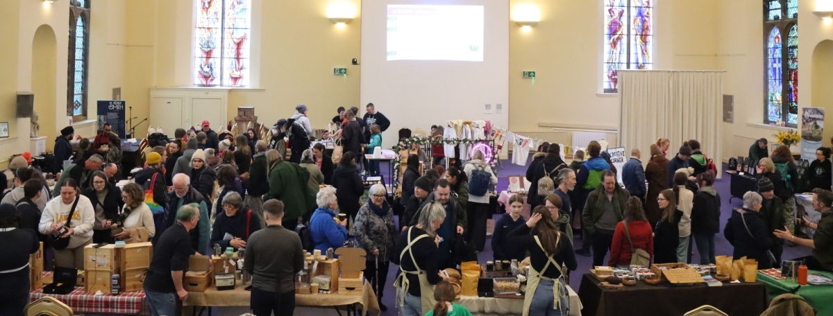 Crowds of people at stalls at an indoor market, with stained glass windows around.